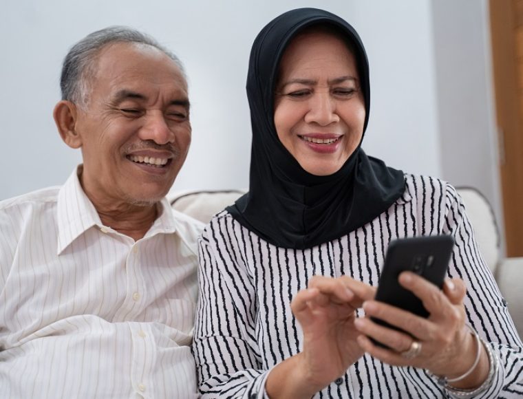 happy senior muslim couple using mobile phone in living room. old asian people